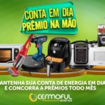 Banner publicitário da campanha Conta em Dia Prêmio na Mão da Cermoful Energia mostrando diversos eletrodomésticos sobre um pedestal dourado em fundo verde.