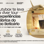 Anúncio publicitário da Beautybox sobre uma promoção que oferece uma viagem com tudo pago para conhecer a fábrica do Grupo Boticário. A imagem destaca um avião dourado sobrevoando uma mala aberta com perfumes, passaporte e frascos de laboratório.