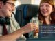 Homem e mulher brindam com copos de vidro em um voo da KLM em anúncio da promoção para o King's Day 2026 em Amsterdã.