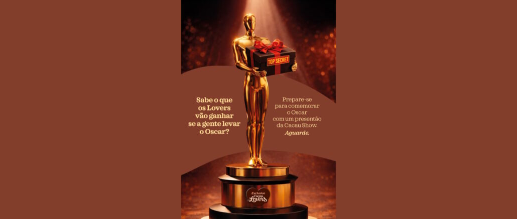 Promoção Oscar Cacau Lovers Cacau Show Estátua dourada similar ao Oscar segurando uma caixa de presente preta com laço vermelho e etiqueta escrita Top Secret em fundo marrom com luzes brilhantes.