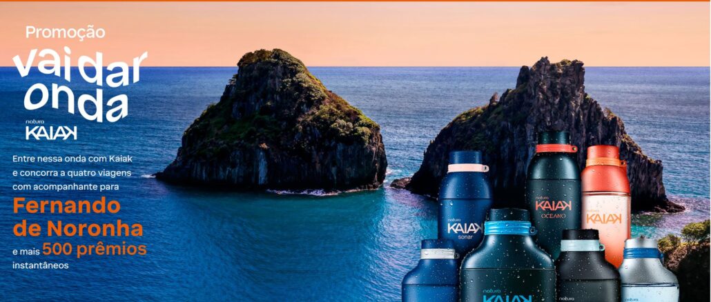 Promoção Vai dar Onda Kaiak Banner promocional da Natura Kaiak intitulado Vai dar onda. A imagem apresenta frascos de perfumes da linha Kaiak em primeiro plano, posicionados à direita. Ao fundo, destaca-se uma paisagem paradisíaca de Fernando de Noronha com formações rochosas no mar e um céu em tons de pôr do sol. O texto à esquerda detalha a promoção.