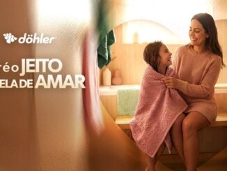 Propaganda de Dia das Maes da marca Dohler. Uma mae sorridente abraça sua filha pequena que esta enrolada em uma toalha rosa. Ao lado esquerdo esta escrito: Cuidar e o jeito dela de amar.