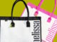 Duas bolsas Melissa Shopper, uma branca com detalhes pretos e outra branca com detalhes rosas, posicionadas sobre um fundo verde.