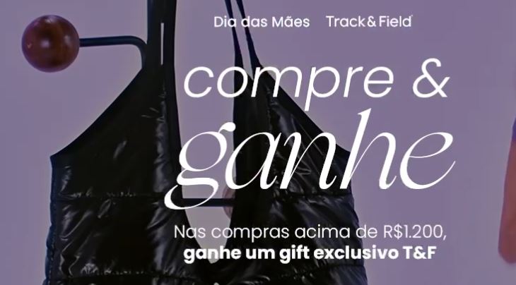 Dia das Mães Track Field 2026 Banner promocional de Dia das Mães da marca Track & Field com o texto Compre & ganhe em destaque sobre a imagem de um acessório esportivo preto acolchoado.