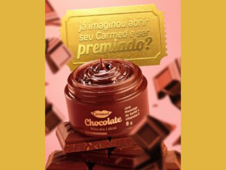Imagem promocional da máscara labial Carmed Chocolate. O produto está em um pote marrom aberto sobre barras de chocolate, com pedaços de chocolate flutuando ao fundo. No topo, um bilhete dourado traz uma mensagem sobre premiação.