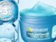 Pote azul aberto de Garnier Hialurônico Toque Seco com gel azul claro e selo indicando sensação de menos três graus Celsius sob fundo com bolhas de água.