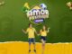 Casal vestindo camisetas da seleção brasileira de futebol celebra animado sob o logotipo da promoção Amor Premiado Flávios, em fundo verde com elementos esportivos como bola de futebol, chuteira, apito e troféu.