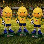 Cinco bonecos colecionáveis do mascote Canarinho Pistola posicionados sobre gramado de estádio segurando latas de Guaraná Antarctica e bolas de futebol.