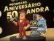 Banner da Promoção Aniversário 50 Anos Andra com mascote técnico em uniforme vermelho e colagem de fotos de viagens pelo Brasil.