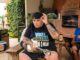Homem tatuado tocando banjo em área de churrasco, com amigos ao fundo usando camisas do Brasil, caixa térmica Brazilna e frasco de Molho do Chefe sobre a mesa, sob o texto "Você e sua galera tem o molho?"