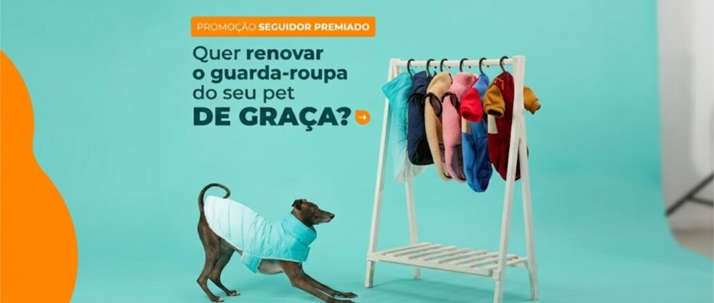 Cachorro de pelagem escura vestindo um colete azul claro se alonga em direção a uma arara de madeira com diversas roupas coloridas para animais em um fundo azul turquesa.