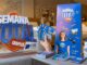 Material de divulgação da campanha Semana Total Chapecó 2026, organizada pela CDL Chapecó, com logotipo tridimensional, banner, folhetos, squeeze e celular sobre uma mesa.