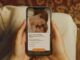 Mãos femininas seguram um smartphone exibindo a campanha de Dia das Mães da Natura, com a mensagem "o tempo passa, o cuidado fica" e a opção de criar um filme personalizado com fotos e vídeos.