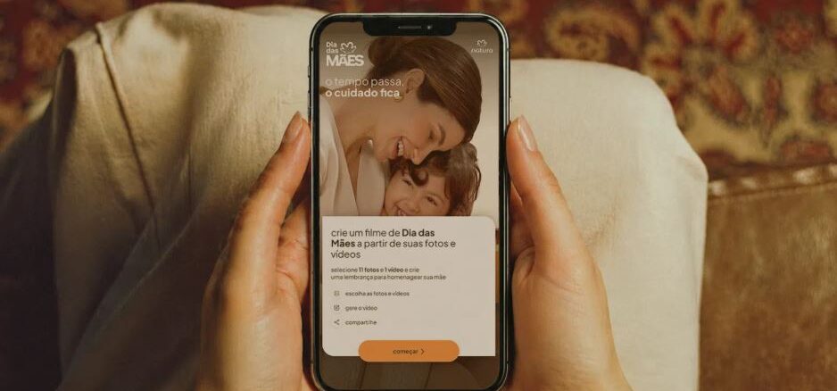 Mãos femininas seguram um smartphone exibindo a campanha de Dia das Mães da Natura, com a mensagem "o tempo passa, o cuidado fica" e a opção de criar um filme personalizado com fotos e vídeos.