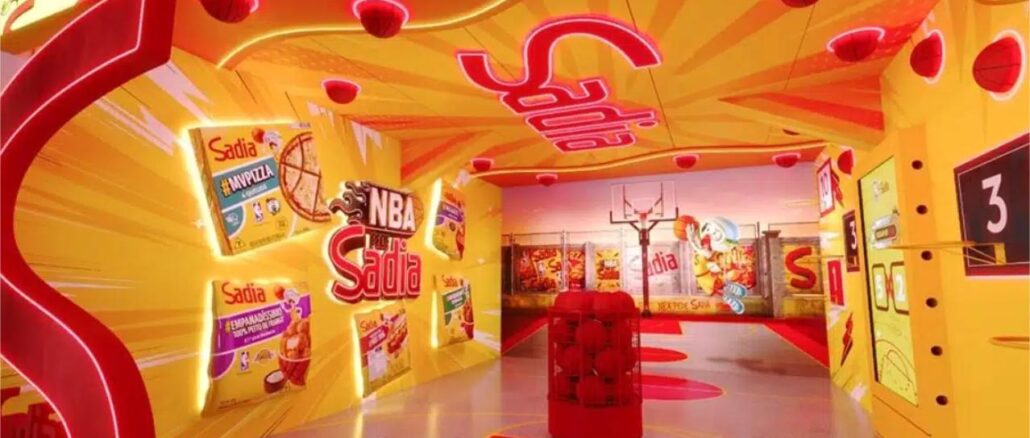 Espaço de ativação da marca Sadia em parceria com a NBA, decorado com as cores amarelo e vermelho, exibindo embalagens de produtos da marca e elementos do basquete.