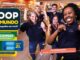 Funcionários da Coop celebram a promoção Coop do Mundo em ambiente de supermercado, com braços erguidos e expressões de alegria, ao lado de arte com informações sobre sorteio de 66 camisas.