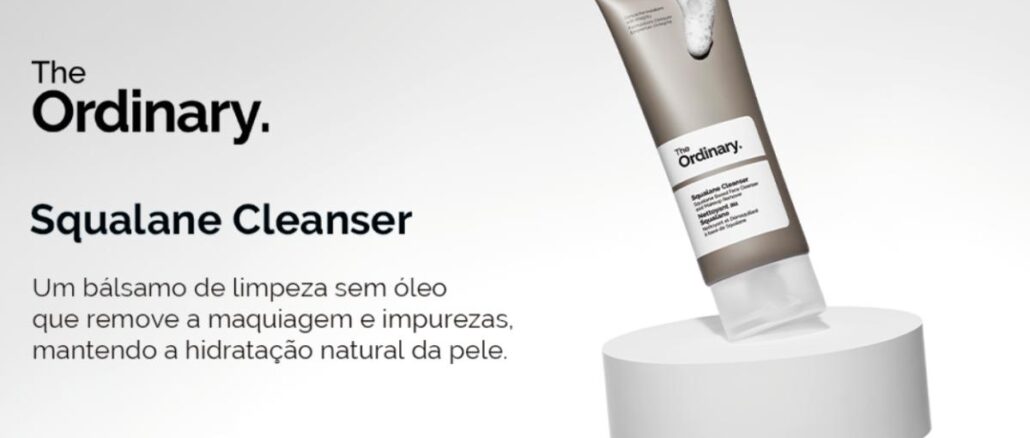 Tubo do Squalane Cleanser da The Ordinary com espuma branca saindo da abertura, apoiado sobre um pedestal cilíndrico cinza claro, ao lado do texto que descreve o produto como um bálsamo de limpeza sem óleo.