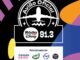 Selo preto e branco com avião estilizado sobrevoando ondas, texto "Avião Oficial" em arco, logo da Rádio Disney 91.3 no centro e faixa branca inferior com os patrocinadores Casas Bahia, Tang, CVC e Rádio Disney sobre fundo colorido com formas geométricas em roxo, laranja, azul e amarelo.