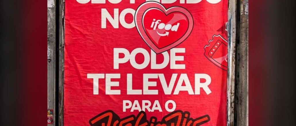 Ifood é Tudo Pra Mim no Rock In Rio 2026 Cartaz vermelho colado em muro anuncia que pedidos feitos pelo iFood podem levar o cliente ao festival Rock in Rio 2026, com o coração do logotipo do iFood ao centro e um ingresso ilustrado ao lado direito.