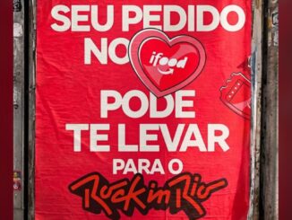 Cartaz vermelho colado em muro anuncia que pedidos feitos pelo iFood podem levar o cliente ao festival Rock in Rio 2026, com o coração do logotipo do iFood ao centro e um ingresso ilustrado ao lado direito.