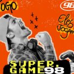 Homem comemora com o punho erguido usando boné e segurando controle de videogame, fundo laranja com ilustrações de bola de futebol e raios, logotipo da 98FM e texto Super Game 98