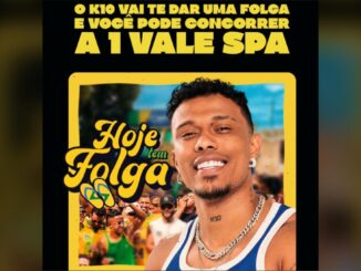 Homem sorridente com corrente e brinco posa em frente a arte da campanha Hoje Tem Folga do K10, com fundo de torcedores em festa de verde e amarelo e texto anunciando sorteio de vale spa