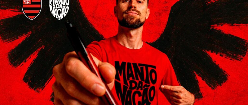 Homem com barba veste camiseta vermelha escrita Manto da Nação, aponta caneta para a câmera, com escudo do Flamengo e logo Manto da Nação ao fundo vermelho com asas negras