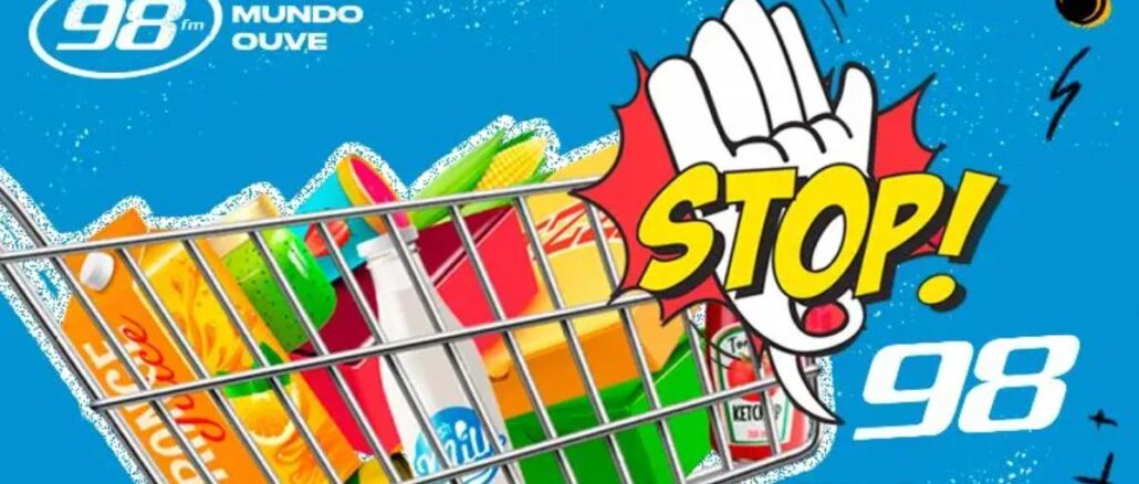 Banner azul da Promoção Stop 98FM Curitiba mostrando um carrinho de compras cheio de produtos alimentícios e de limpeza, com uma mão em formato de sinal de pare e a palavra STOP em amarelo ao lado do logotipo da rádio 98FM.