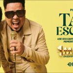 Dois cantores sorrindo com microfones dourados nas mãos, ao lado de um cartão BB Elo dourado, anunciando a promoção Tava Escrito com prêmio de R$1.000.000,00 em certificados de barras de ouro
