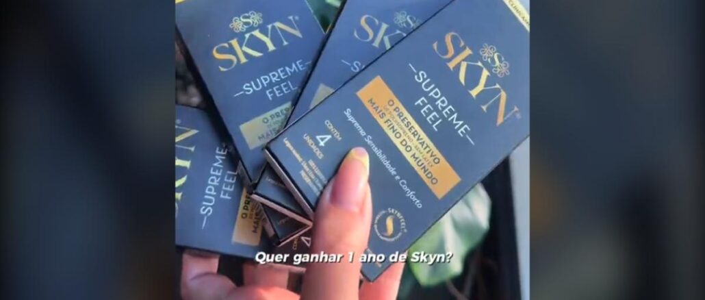 Skyn Cam Sinta Tudo, Durante e Depois do Jogo Mão feminina segurando várias caixas azuis do preservativo Skyn Supreme Feel com o texto sobreposto "Quer ganhar 1 ano de Skyn?"