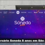 Painel do Aniversário Soneda 8 Anos com logotipos de marcas parceiras como Nivea, Pantene, Neutrogena e outras, em fundo roxo com confetes coloridos.