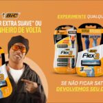 Ronaldinho Gaúcho segura um aparelho de barbear BIC Flex3 e aponta para ele, ao lado de embalagens dos modelos Flex3 Recarregável, Flex3 e Flex3 Sensitive, com a oferta "Barbear extra suave ou seu dinheiro de volta"