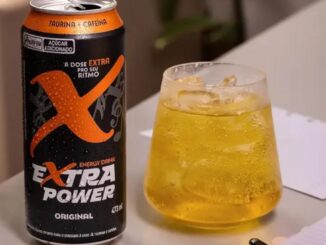 Lata de energy drink Extra Power Original 473ml ao lado de um copo com gelo e bebida amarelada, sobre superfície clara.