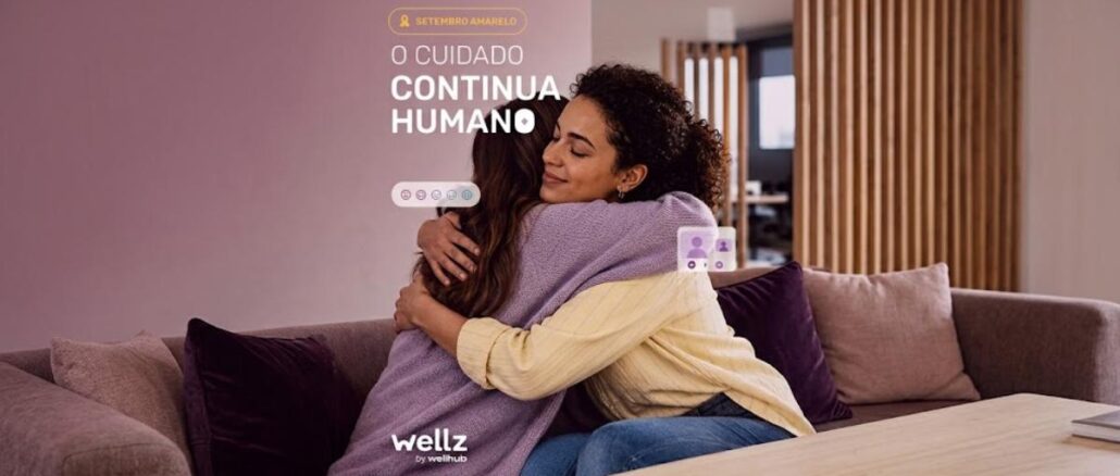 Promoção Wellz Setembro Amarelo_ a gente se cuida! Duas mulheres se abraçam afetuosamente em um sofá, com a frase "O Cuidado Continua Humano" e a marca Wellz by Wellhub sobrepostas à imagem, em campanha do Setembro Amarelo.