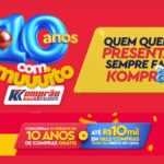 Banner da campanha de aniversário de 10 anos do Komprão Koch Atacadista em Santa Catarina, com fundo vermelho, balões azuis e vermelhos e destaque para os prêmios de 10 anos de compras grátis e até R$10 mil em vale-compras todo dia.