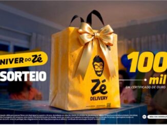 Sacola dourada do Zé Delivery com laço de fita dourada sobre uma mesa, ao lado do texto "Niver do Zé – Sorteio 100 mil em Certificado de Ouro".