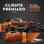Arte da promoção Cliente Premiado Stihl com o slogan 100 anos de história, 100 prêmios para você, exibindo um Ford Bronco laranja, motocicleta, bicicleta elétrica, patinete elétrico, frigobar, caixa de som JBL, smartphone, smartwatch e notebook, todos em tons de laranja sobre fundo escuro.