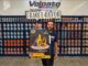 Funcionário da Volpato Tintas segura cartaz do Concurso Craque da Cor em loja de Maringá, Paraná