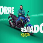 Entregador sorridente com jaqueta verde da Keeta, de braços cruzados ao lado de uma motocicleta azul, sobre fundo verde com o título Corre Premiado Keeta.