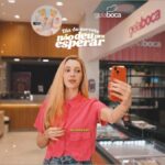 Jovem segurando celular laranja dentro de loja Gela Boca, com texto "Dia do sorvete não deu pra esperar" em destaque.