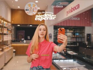 Jovem segurando celular laranja dentro de loja Gela Boca, com texto "Dia do sorvete não deu pra esperar" em destaque.