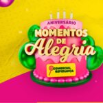 Arte da promoção Aniversário Momentos de Alegria da Comercial Esperança, com bolo rosa de dois andares, velas acesas e balões metálicos verdes e rosa sobre fundo amarelo e rosa.