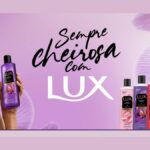 Banner da promoção Sempre Cheirosa com Lux, com mulher de cabelos cacheados segurando um sabonete líquido Lux Orquídea Negra e cinco frascos da linha Lux ao lado, com selo indicando que Lux Líquido dobra as chances no sorteio.