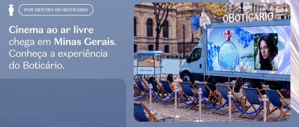 Cinema ao ar livre do Boticário em Belo Horizonte, com caminhão-telão exibindo o perfume Floratta, carrinho de pipoca e espectadores sentados em cadeiras de praia azuis diante de prédio histórico.