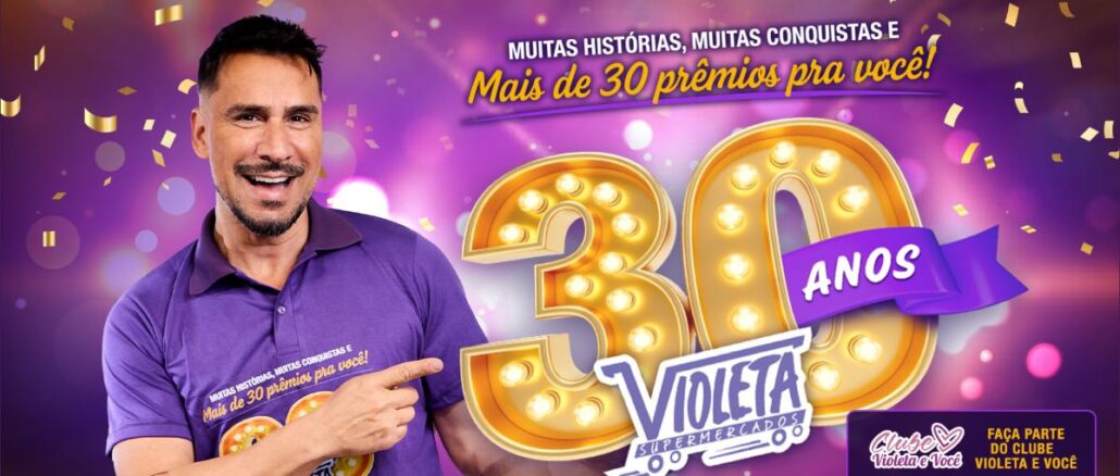 Supermercados Violeta 30 anos de História em São Paulo Homem sorridente com camisa roxa aponta para o número 30 dourado com lâmpadas e o logotipo dos Supermercados Violeta, ao lado do texto "Mais de 30 prêmios pra você!".