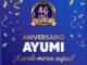 Arte da promoção Aniversário Ayumi – A Sorte Mora Aqui, com selo dourado de 46 anos do Ayumi Supermercados sobre fundo azul com serpentinas e confetes dourados.
