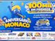 Cartaz da promoção Aniversário Monaco, do Monaco Atacado, com mascote azul em forma de letra M usando chapéu de festa e o anúncio de 100 mil em prêmios no Clube de Desconto, com logos dos patrocinadores no rodapé.