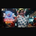 Homem de óculos escuros e camisa de palmeiras aponta para a câmera em um supermercado, ao lado do logotipo da promoção Armazém Acelera, com carrinho de compras, carros e televisores, e o slogan "Seu carrinho vai virar carrão!".