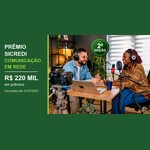 Banner do Prêmio Sicredi Comunicação em Rede, 2ª edição, com R$220 mil em prêmios e inscrições até 31/07/2027, ao lado de um homem e uma mulher gravando um podcast com fones de ouvido, microfones e câmera.