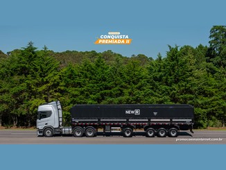 Caminhão prata com semirreboque graneleiro preto da Linha New R diante de uma mata verde, sob o selo "Promoção Conquista Premiada II".